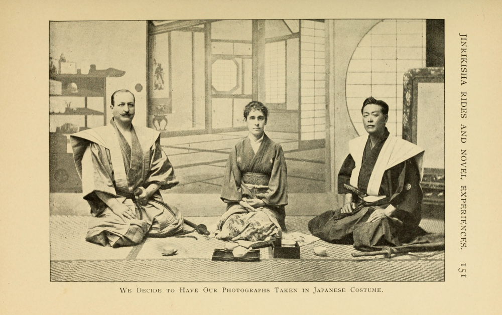 Two man and a woman dressed in historical Japanese clothing, seated on a mat.