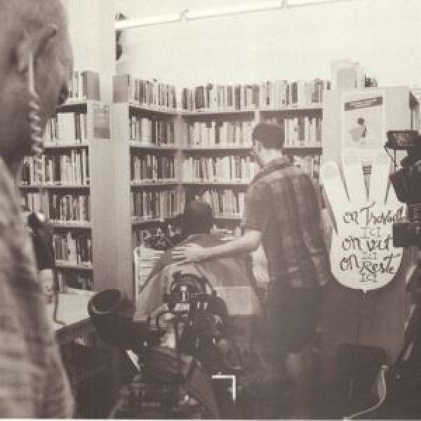 Man seated with back to camera, another man standing beside him with his arm around him.